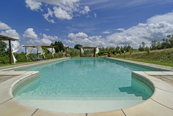A clear swimming pool with a pergola and lounge chairs.