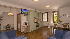 Ein gemütliches Wohnzimmer mit Fernseher, ein Essbereich mit Tisch und Stühlen sowie eine Küche mit grünen Schränken und einer Mikrowelle.
