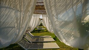 A row of sun loungers under white canopies in a garden setting.