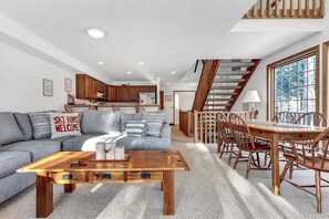 A modern living room with a sofa, coffee table, and dining area with chairs and a staircase. - Powder Ridge Townhouse 33 (Newry)