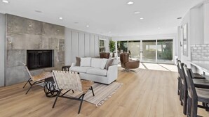 A spacious living room with a fireplace, a sofa, and a dining area with a table and chairs. - @ Marbella Lane - 3BR w/sweeping views of Bay Area (San Mateo)