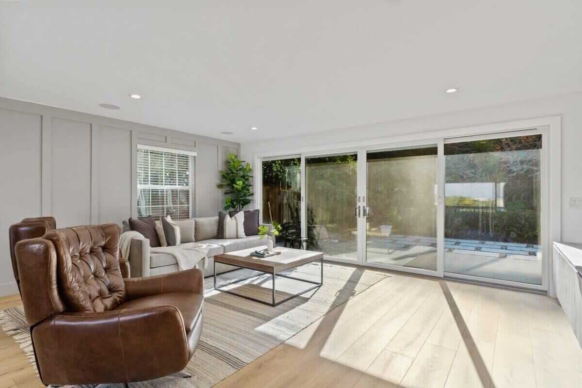 A modern living room with a leather sofa, a coffee table, and a large sliding glass door leading to an outdoor area.