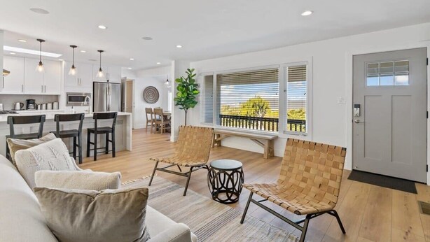A modern living room with a sofa, two woven chairs, a small round table, and a large window with blinds. - @ Marbella Lane - 3BR w/sweeping views of Bay Area (San Mateo)