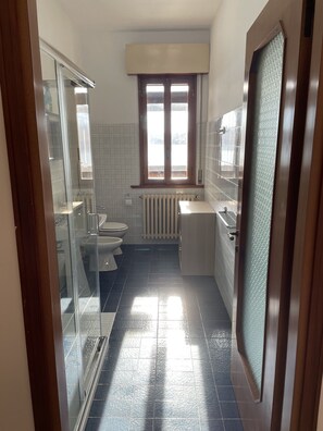A modern bathroom with a glass shower enclosure, a toilet, a sink, and a window above the toilet.