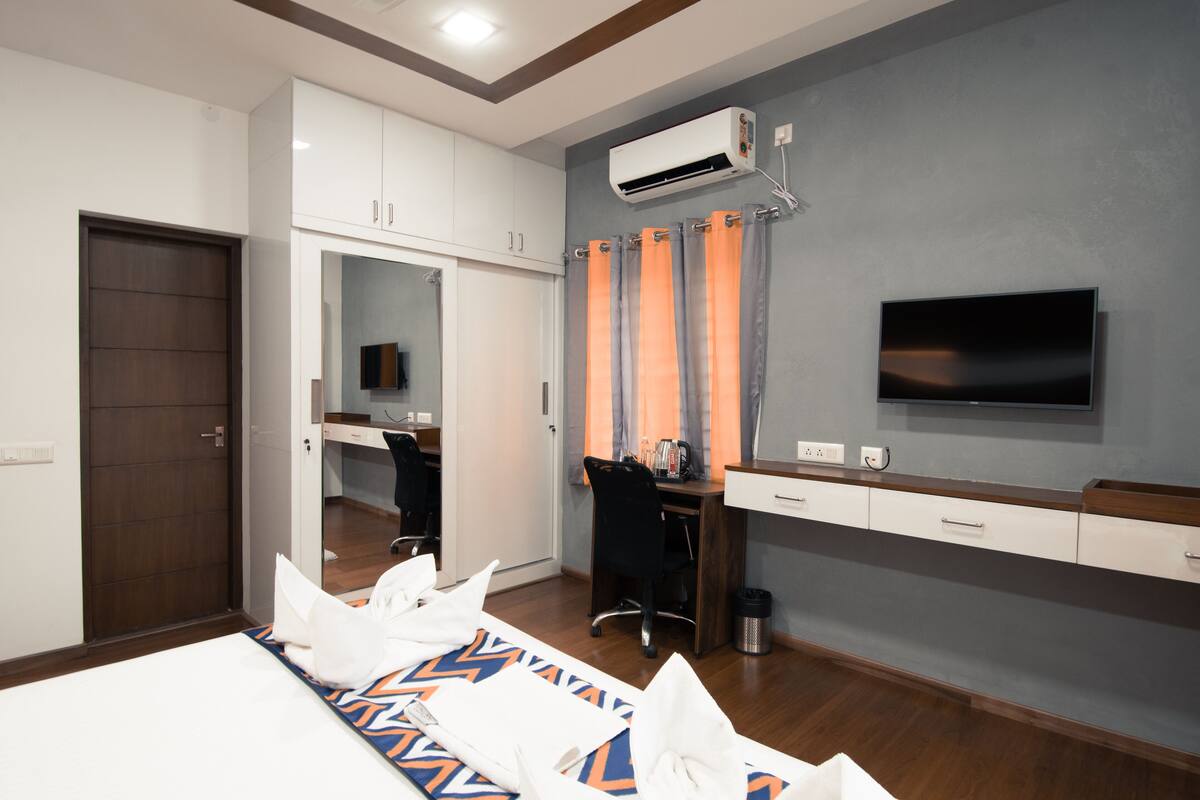 Una habitación de hotel moderna con cama, escritorio, silla, televisor y aire acondicionado.