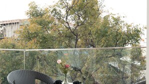 En balkon med et rundt glasbord, to fletstole og en vase med blomster.