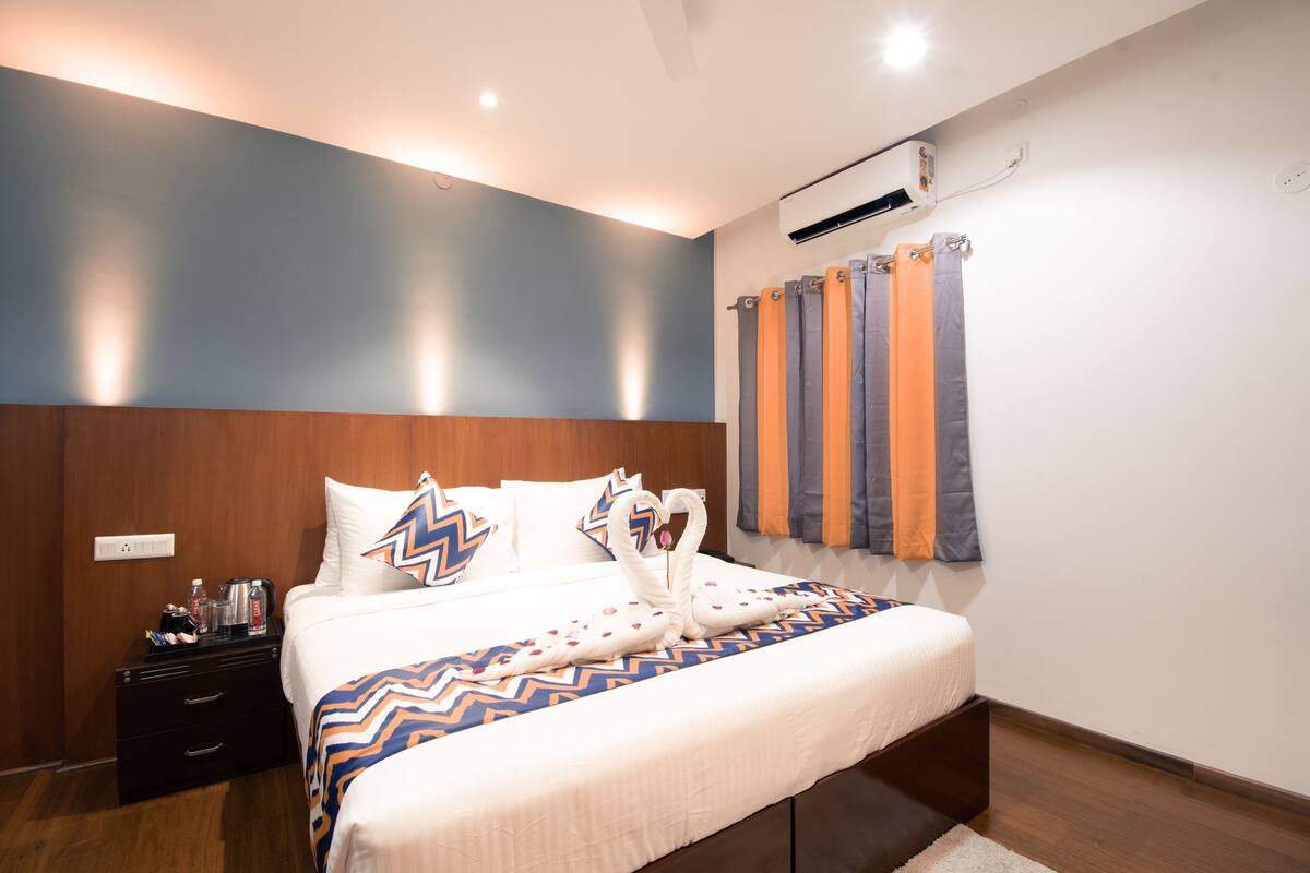 Habitación de hotel con cama, mesita de noche, aire acondicionado de pared y ventana con cortinas.