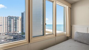 Ett hotellrum med ett stort fönster som erbjuder utsikt över en strand och höga byggnader.