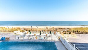 Zona de piscina con sillones reclinables y sombrillas, área de playa cercada y vista despejada al océano.