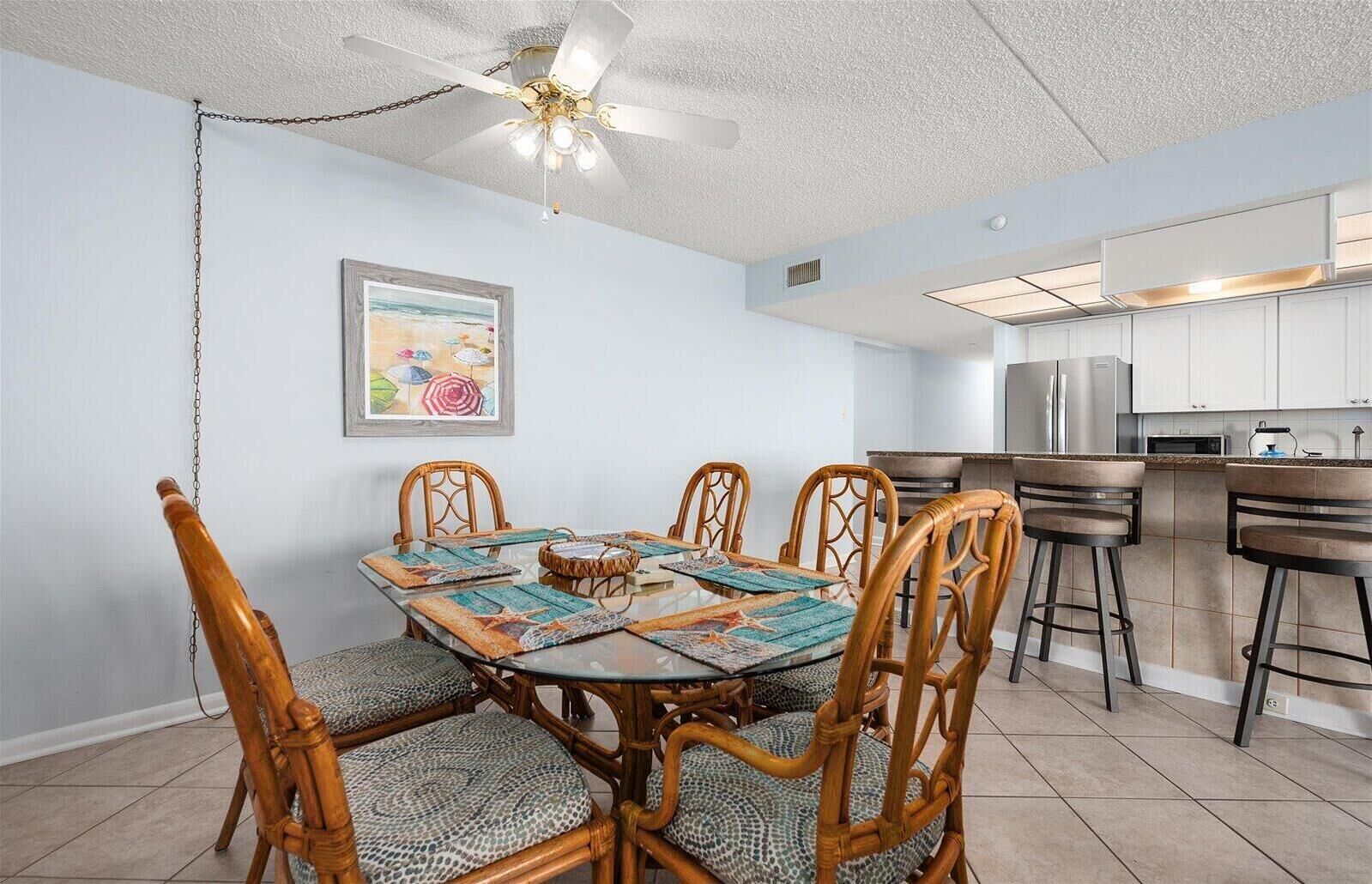 A dining area with a round table, six chairs, and a ceiling fan.