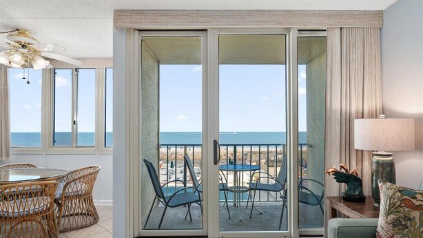 Un balcón con vista a la playa, sillas de mimbre, una mesa y una lámpara.