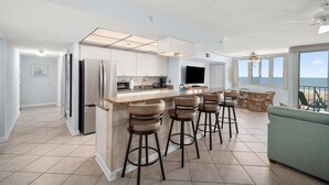 Una cocina moderna con una isla central, taburetes de bar y un amplio ventanal con vista al océano.