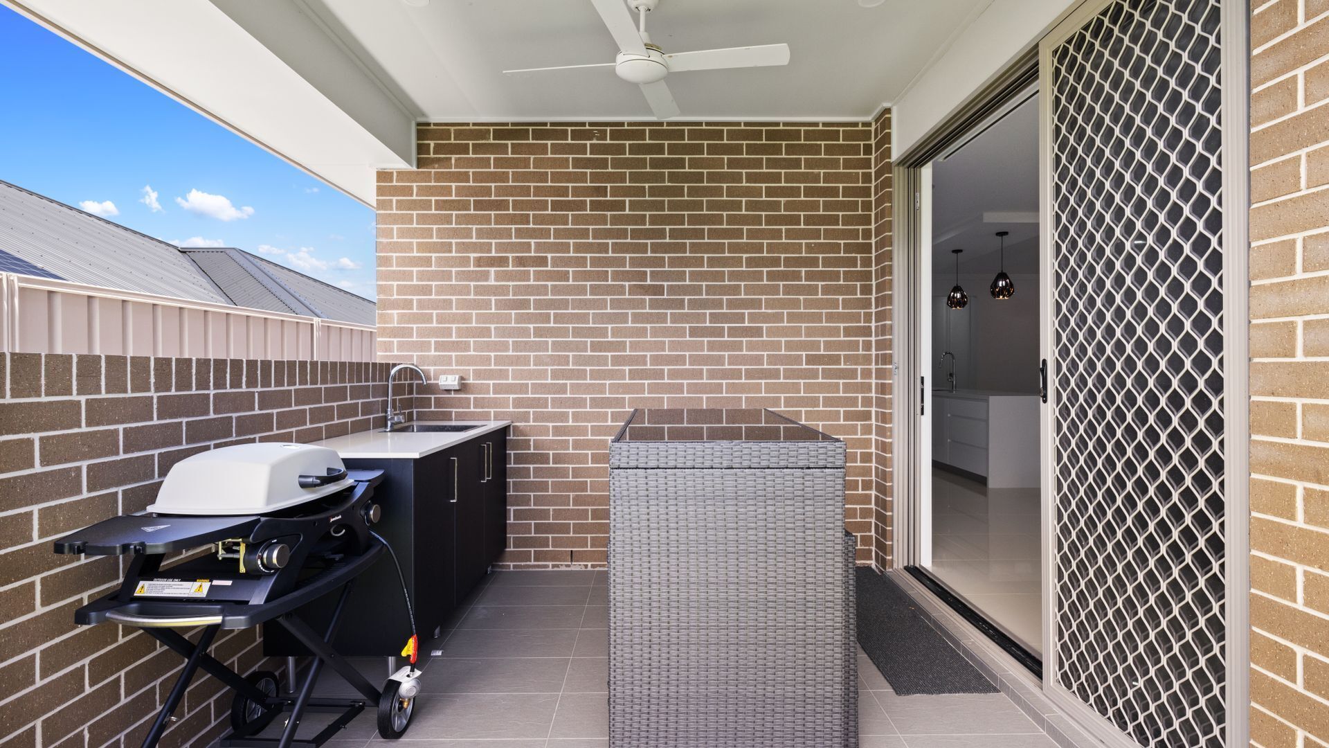 Un patio con una parrilla, un lavamanos pequeño y una puerta que da a un espacio interior.
