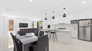 A modern kitchen with white cabinets, a stainless steel refrigerator, and pendant lighting. - Gone Coastal - Comfortable family holiday house (Woolgoolga)
