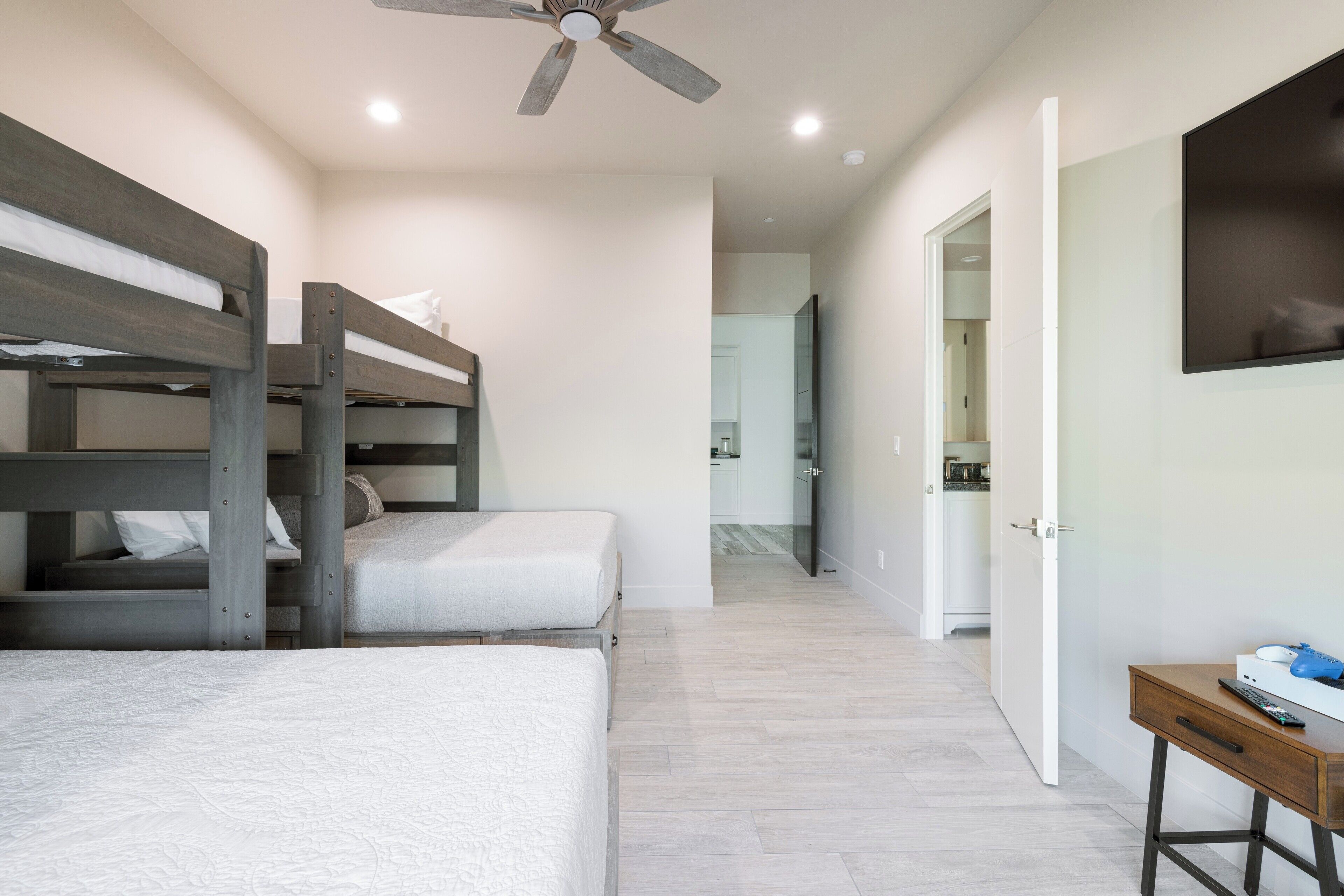 Une chambre avec des lits superposés, un bureau et un ventilateur de plafond.