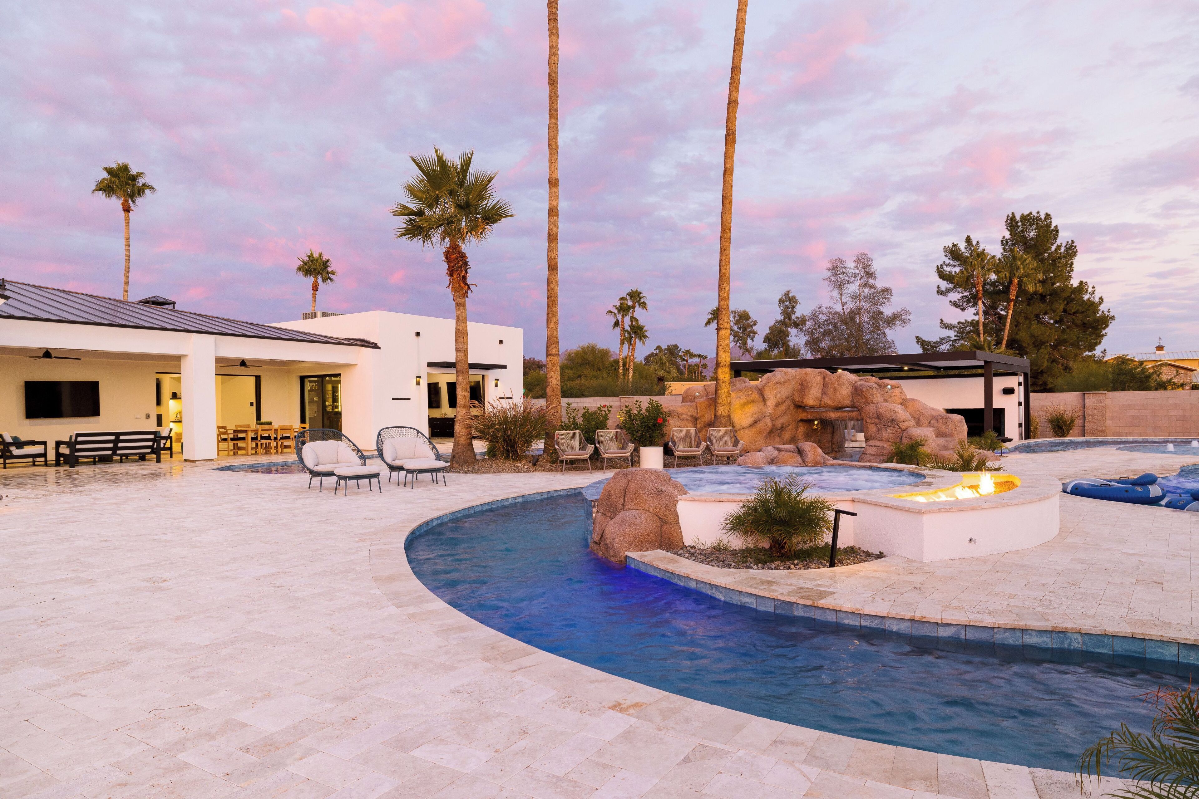 Un área de piscina con un jacuzzi, sillones de descanso y palmeras.