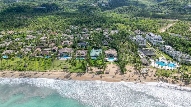 Luftaufnahme eines Resorts mit mehreren Gebäuden, einem Strand und einer gebirgigen Kulisse.