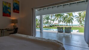 Ein Schlafzimmer mit einem großen Bett, einem Schreibtisch und einem Stuhl. Blick auf einen Pool und Palmen.