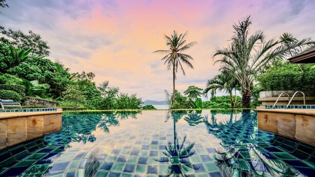A clear pool with a tiled floor and palm trees around. - Glasshouse Phuket | 6BR Villa | Sleeps 22 | Walk to 2 Beaches | Accessible (Vichit, Muang)