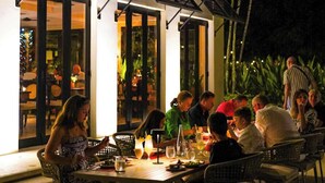 Un espace extérieur aménagé pour les repas, avec des tables et des chaises, un bâtiment doté d’un balcon et un environnement tropical.