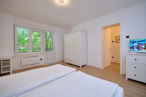 Relax in this serene bedroom with a large bed, a wardrobe, and a TV, offering a view of lush greenery.