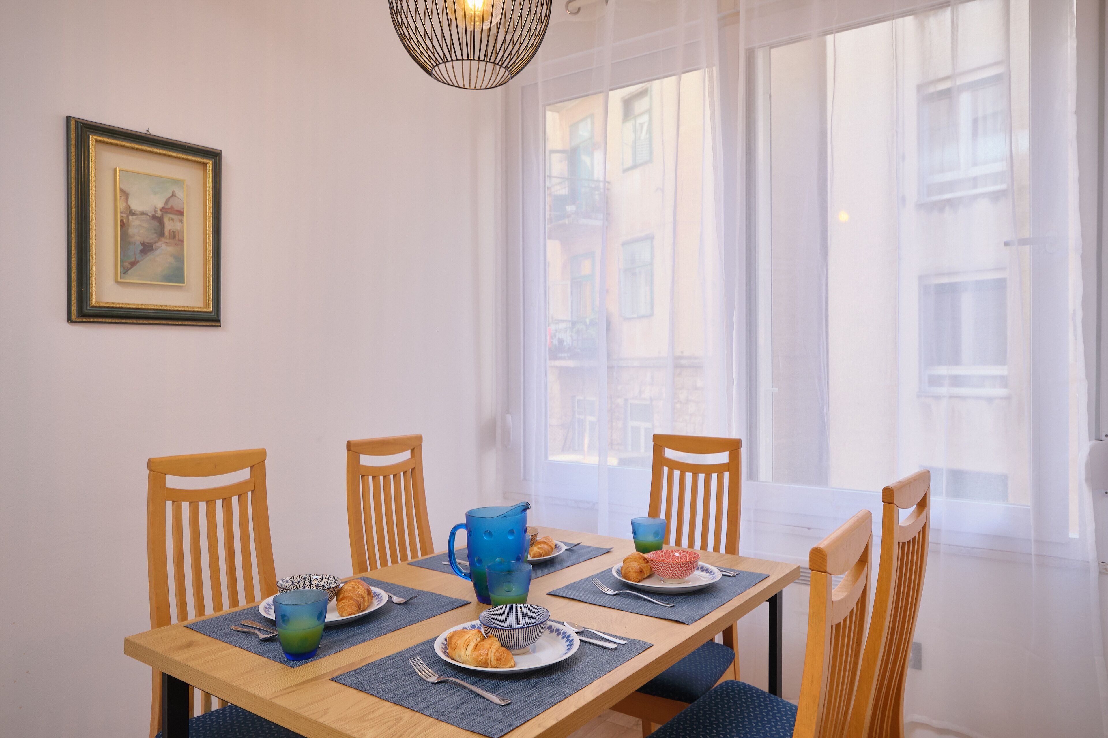 A dining table with four chairs, a pitcher, plates with food, and a framed picture on the wall.