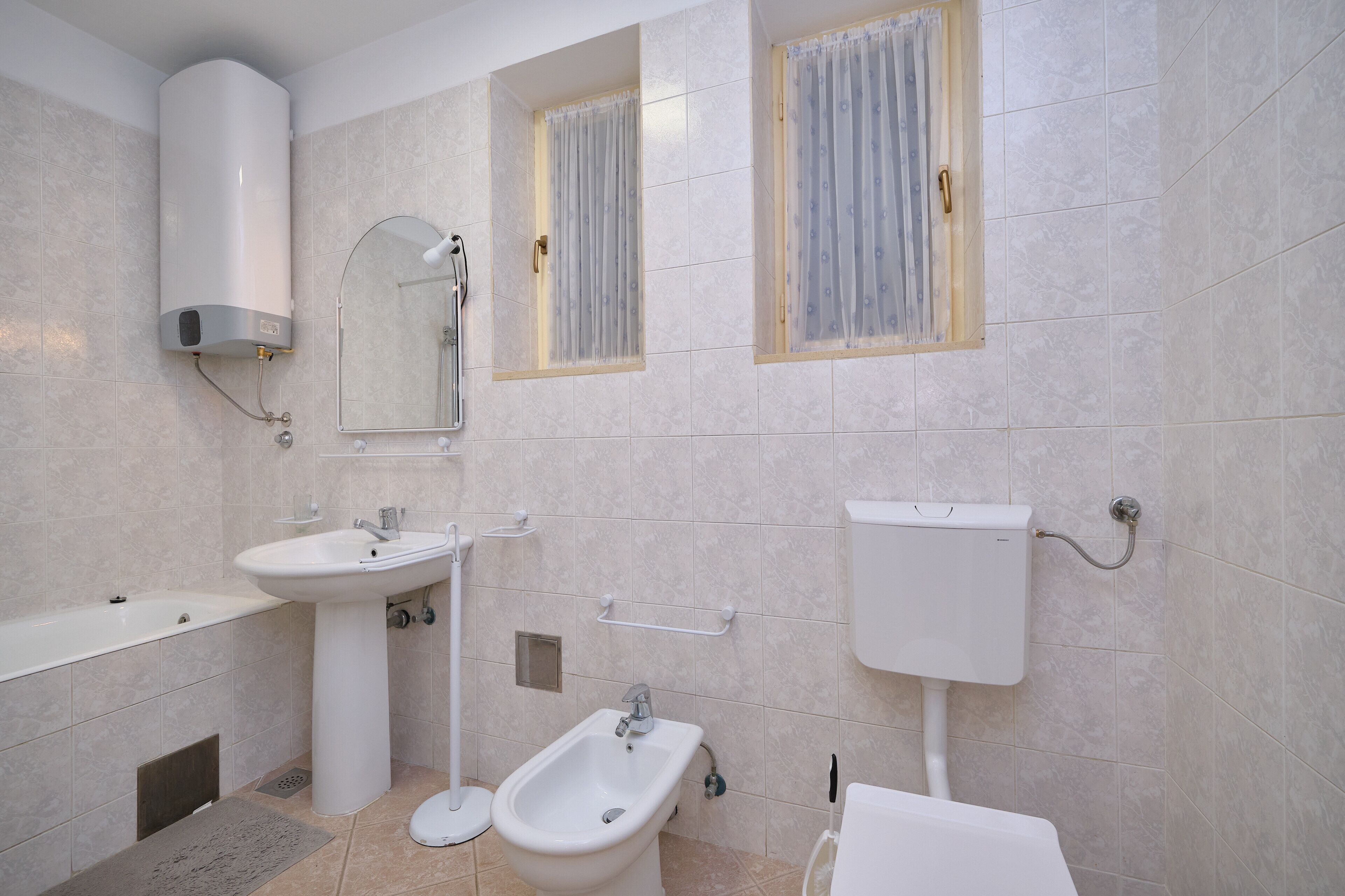 A modern bathroom with a bathtub, sink, bidet, toilet, and a water heater.