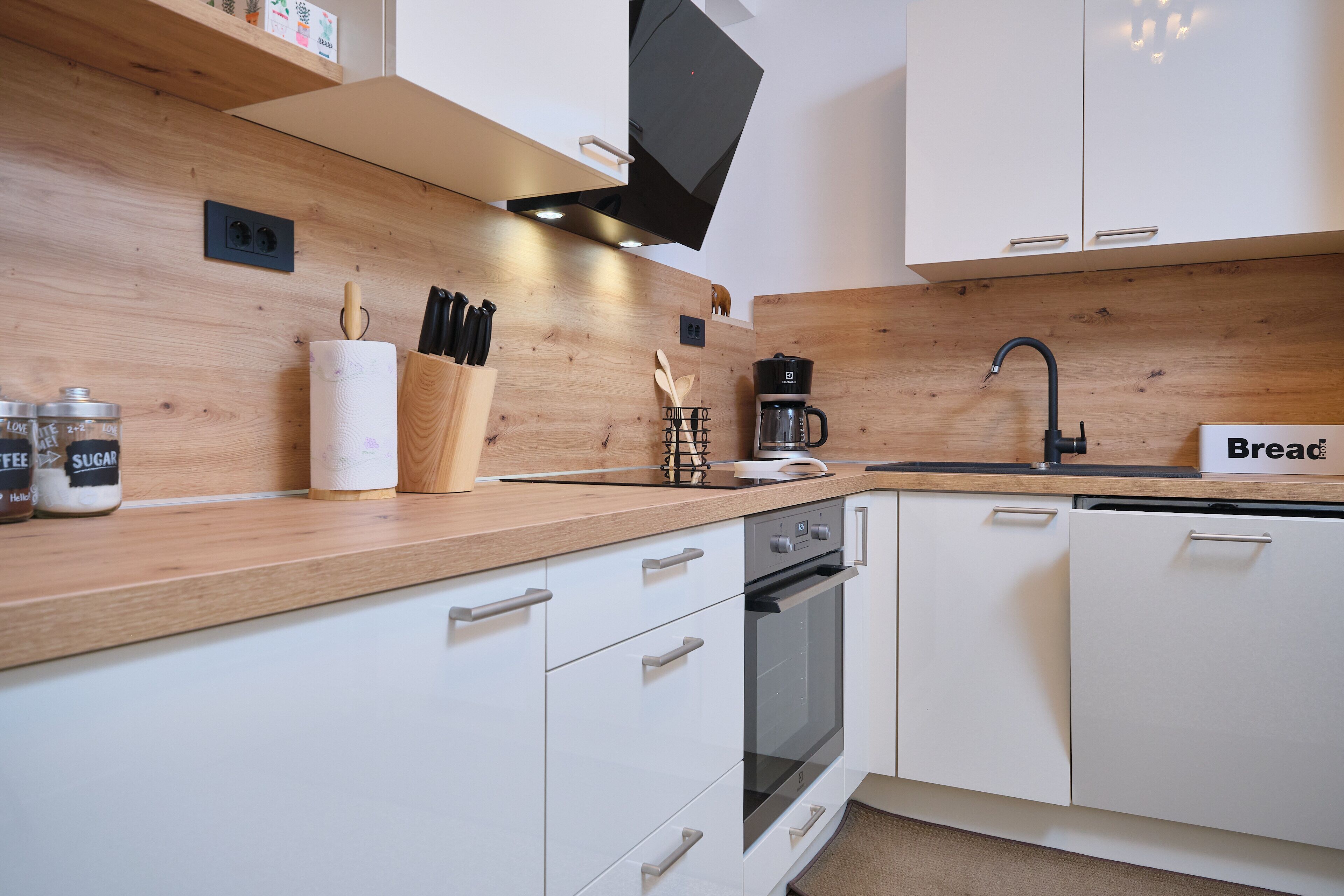 Eine moderne Küche mit weißen Schränken, einer Holz Arbeitsplatte, einer Kaffeemaschine und einer Brotdose.