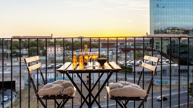A balcony with a table set for two, featuring a bottle of liquor, two glasses, and a bowl. - Camesena 40 | 2BR Apartment for 4 with Balcony near Tiburtina (Roma)
