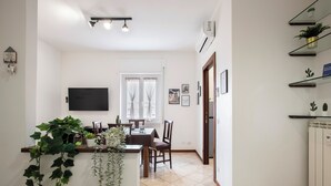 A dining area with a table and chairs, a TV mounted on the wall, and potted plants on a counter. - Camesena 40 | 2BR Apartment for 4 with Balcony near Tiburtina (Roma)