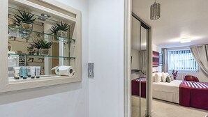 Une salle de bain moderne avec une étagère en verre où sont rangés les articles de toilette et des plantes, des toilettes et un espace douche.