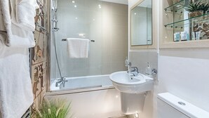Une salle de bain moderne avec une douche à parois de verre, un lavabo blanc et une étagère en verre où sont rangés les articles de toilette.