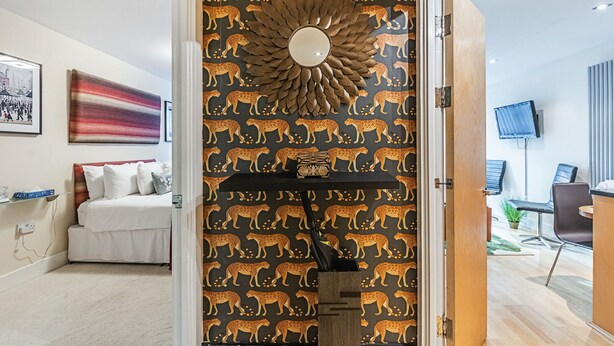 Une chambre d’hôtel avec un papier peint à motifs léopard, un lit, une table de chevet et un téléviseur dans l’espace salon.