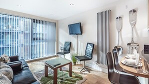 Un salon moderne comprenant un canapé, une table basse, un téléviseur et un coin repas avec des chaises et une table.