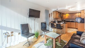 Un salon moderne doté d’un téléviseur, de sièges et d’un coin cuisine.