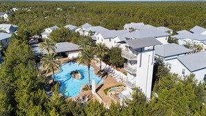 A resort with multiple buildings, a central swimming pool with a rock feature, and surrounding palm trees. - Bluebird Beach House - 3 Kings - Pet Friendly (Santa Rosa Beach)