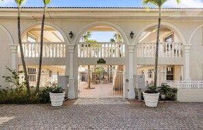 A gated entrance with a white facade, arched balconies, and potted plants. - Castleton Gardens 204 - Olde Naples Prime Location, Newly Renovated! (Naples)