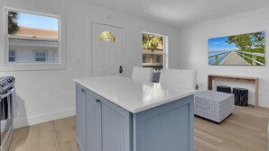 Une cuisine moderne dotée d’un îlot central, de meubles blancs et offrant une vue sur l’extérieur grâce à de grandes fenêtres.