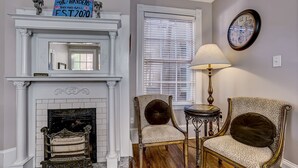 A room with a fireplace, two upholstered chairs, a table, and a clock on the wall. - Classic Jones Street Apartment-Off Street Parking Spot Included! (Savannah)