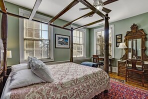 A four-poster bed with white and red bedding, a wooden dresser, and a large mirror in a room with green walls and wooden floors. - Classic Jones Street Apartment-Off Street Parking Spot Included! (Savannah)