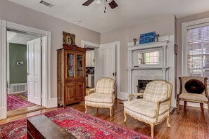 Un salon avec une cheminée, deux fauteuils à motifs écossais, un meuble en bois et un tapis rouge à motifs.