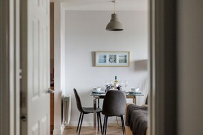 Un comedor con una mesa dispuesta para dos, una lámpara colgante y un cuadro en la pared.