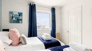 A hotel room with two beds, a large window with curtains, a door, and a wall-mounted artwork.