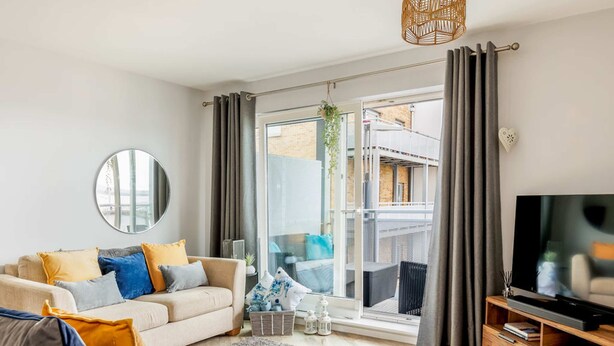 A modern living room with a sofa, TV, and a large window with curtains.