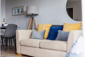 A living room with a beige sofa, a lamp, a chair, and a dining table.