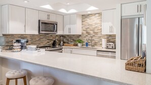 A modern kitchen with white cabinets, a stainless steel refrigerator, a microwave, and a coffee station.