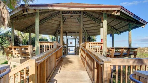 A wooden covered walkway leading to a beach area with benches and a view of the ocean.