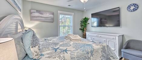 Un dormitorio con cama, ventilador de techo, televisión, planta y ventana.