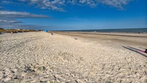 Une plage de sable parsemée d’empreintes, un ciel dégagé et une côte lointaine.