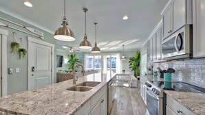 Una cocina moderna con encimeras de granito, electrodomésticos de acero inoxidable e iluminación colgante.